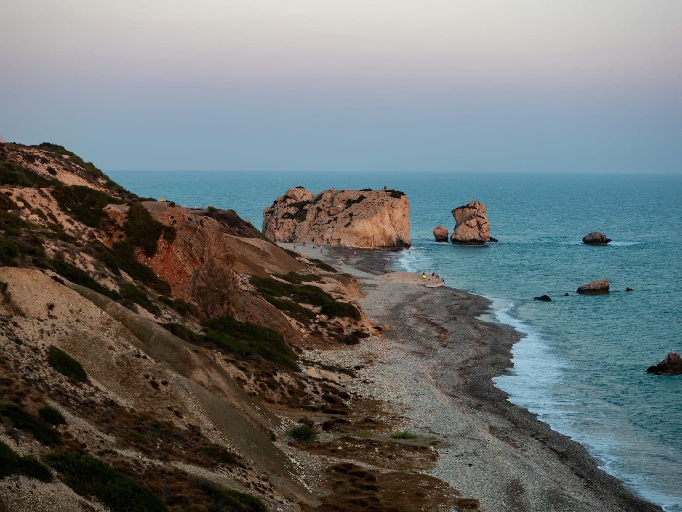 Petra tou Romiou from the cliffs at dusk: the great rock and its smaller stacks off a long pebble beach