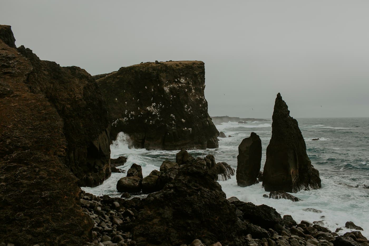 Dark cliffs and sea stacks on the Reykjanes coast, with surf breaking on a grey day