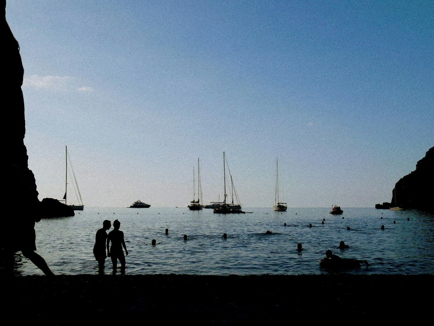 A couple in silhouette at a Mallorcan cove, with sailing boats beyond