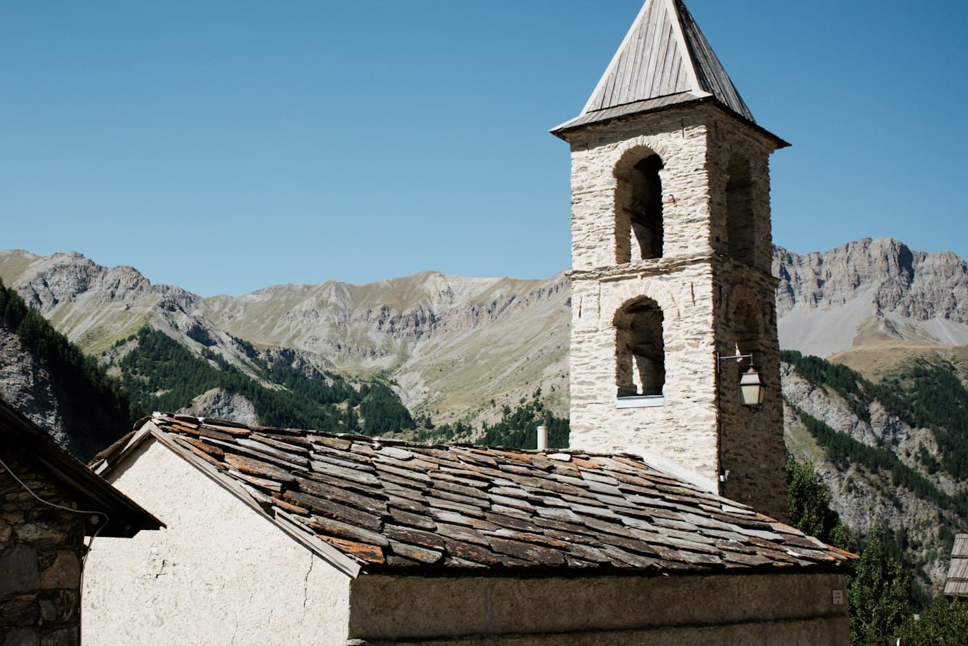 A stone bell tower and slate roof in Saint-Véran, below the mountains