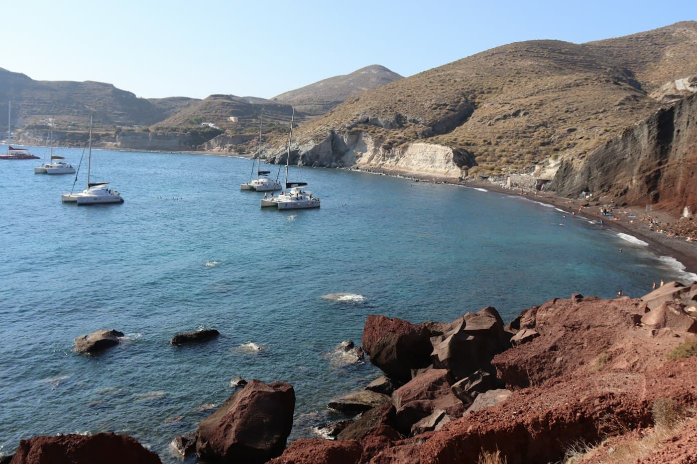 Catamaranes fondeados frente a la Playa Roja, bajo sus acantilados volcánicos rojos y negros, en Santorini