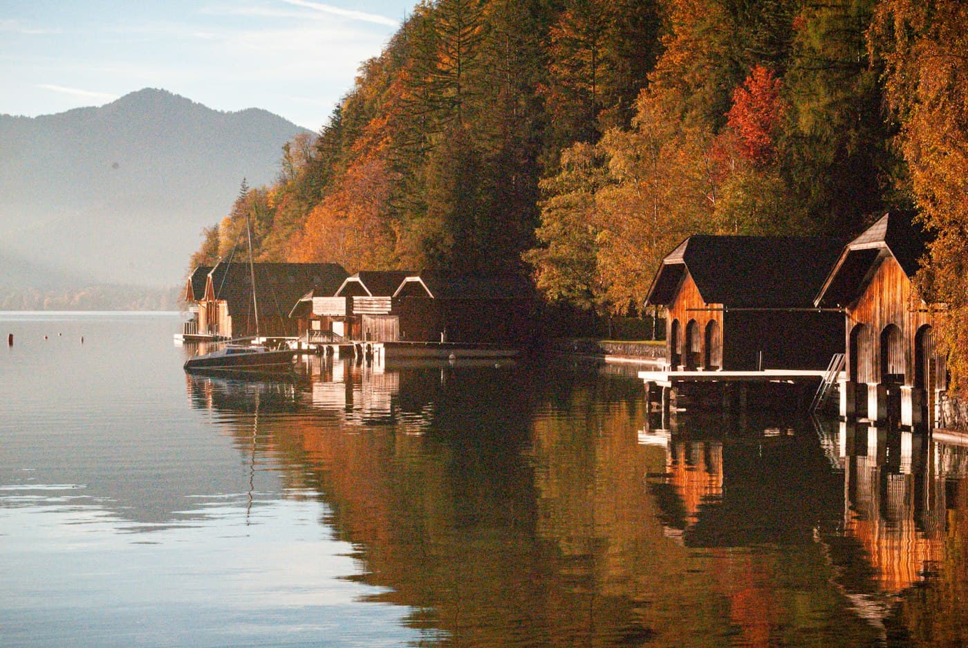 Rimesse per le barche in legno tra gli alberi autunnali a Strobl, sul Wolfgangsee, riflesse nell’acqua immobile