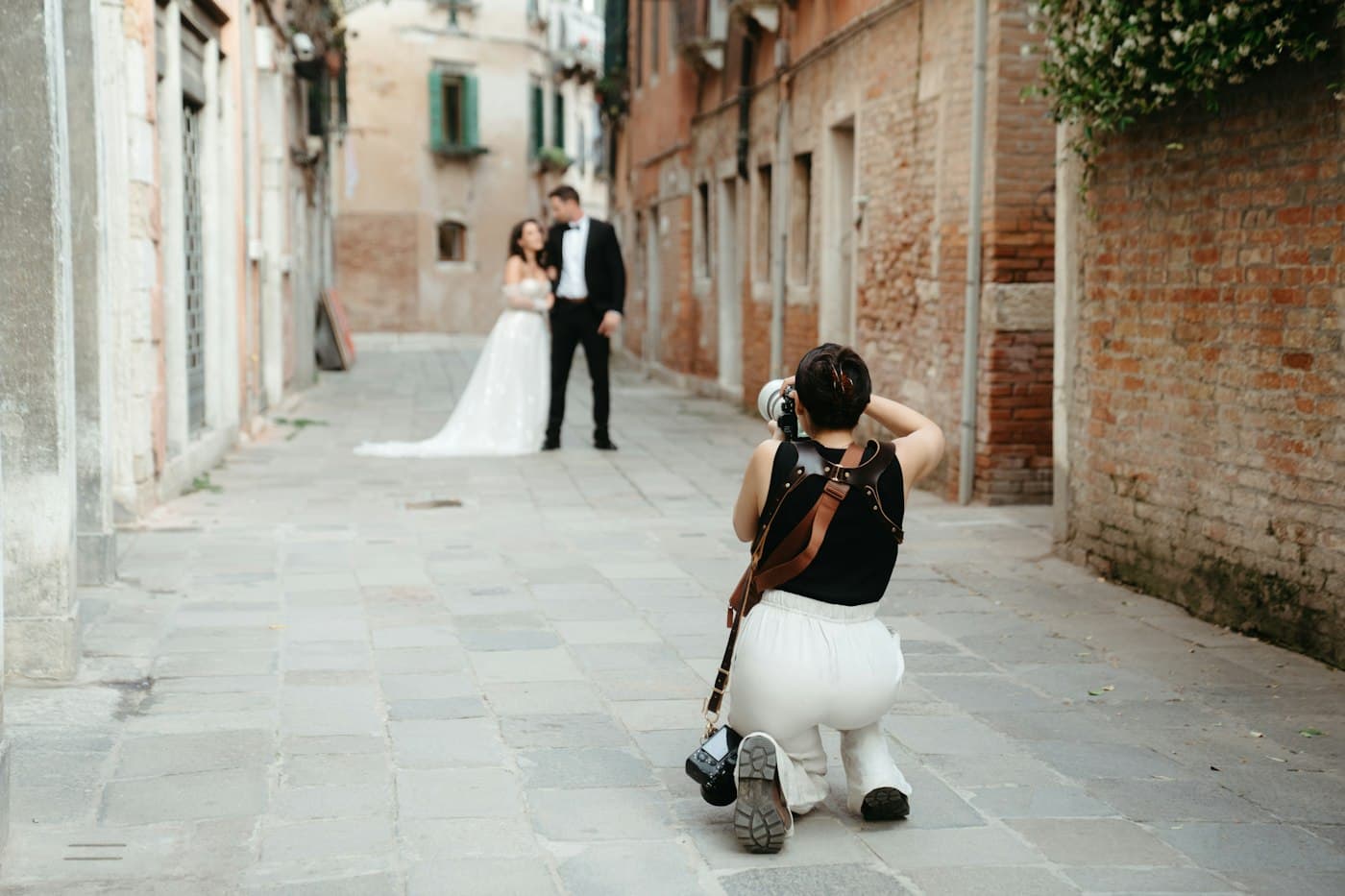 A photographer kneeling to photograph a bride and groom in a Venetian lane