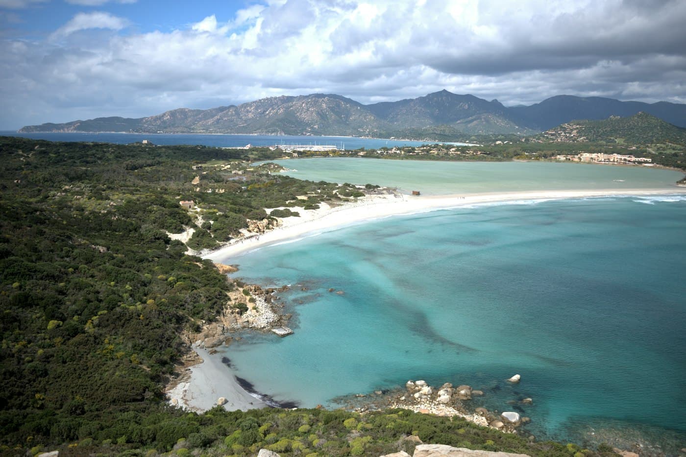 Ein weißer Strand zwischen einer Lagune und dem Meer bei Villasimius, dahinter Berge