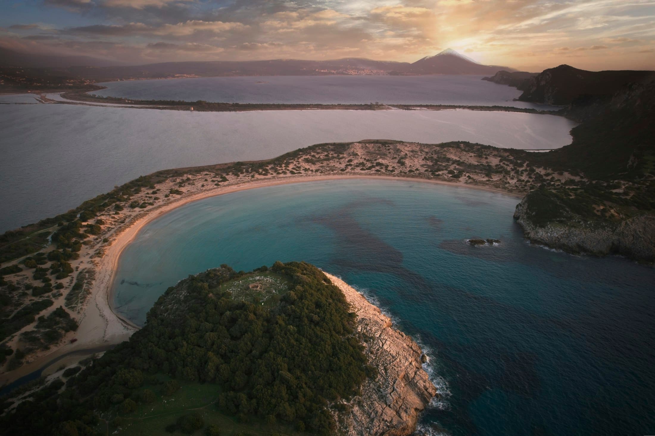 Die runde Bucht von Voidokilia von oben, dahinter die Lagune und die Bucht von Navarino unter einem goldenen Himmel