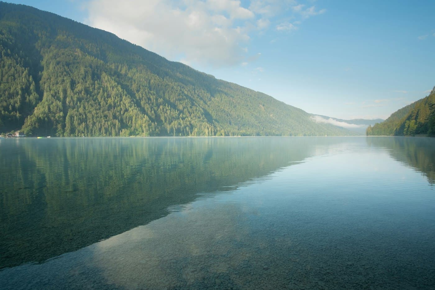 The still Weissensee on an early summer morning, its wooded slopes mirrored in the clear water