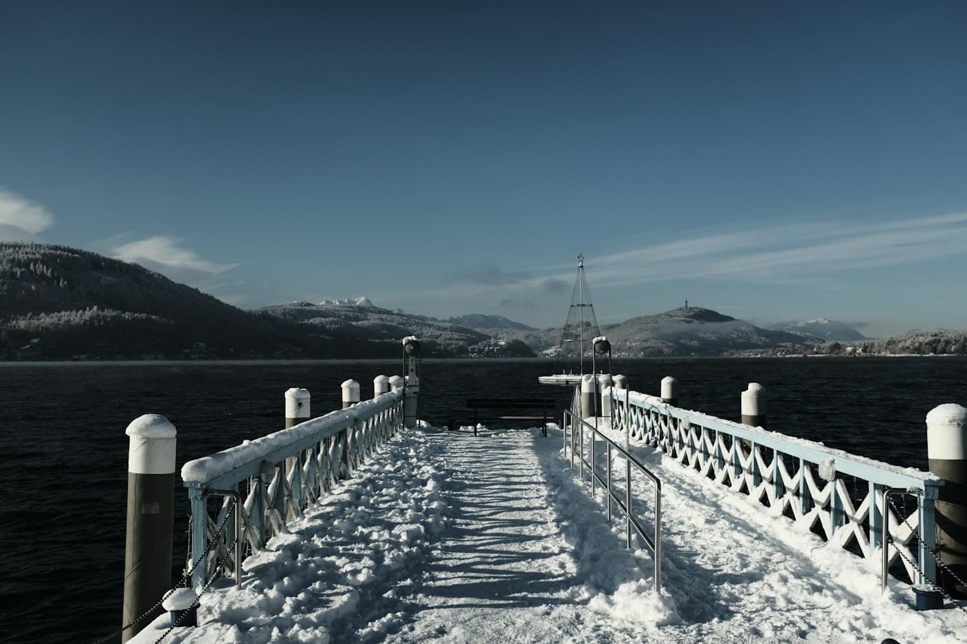 A snow-covered landing stage reaching into the Wörthersee on a clear winter day