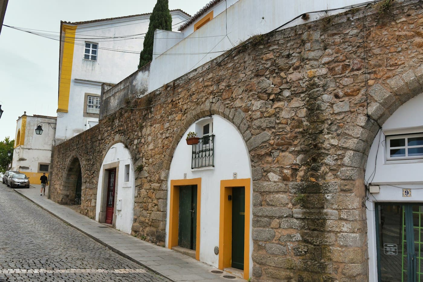 Casas construídas nos arcos do antigo aqueduto de Évora: paredes brancas, portas com molduras amarelas e pedra de granito