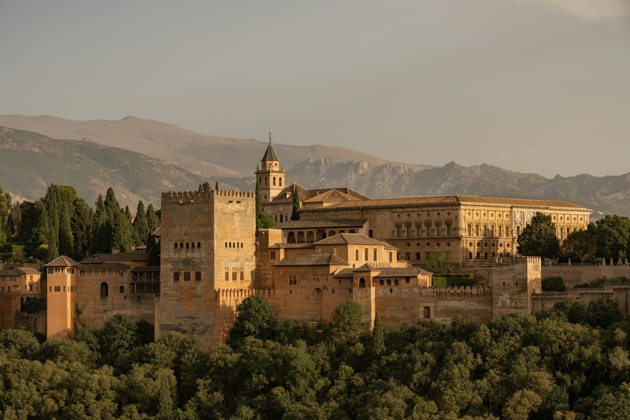 The Alhambra in golden evening light: the Comares tower, the Palace of Charles V and the bell tower of Santa María, the Sierra Nevada behind