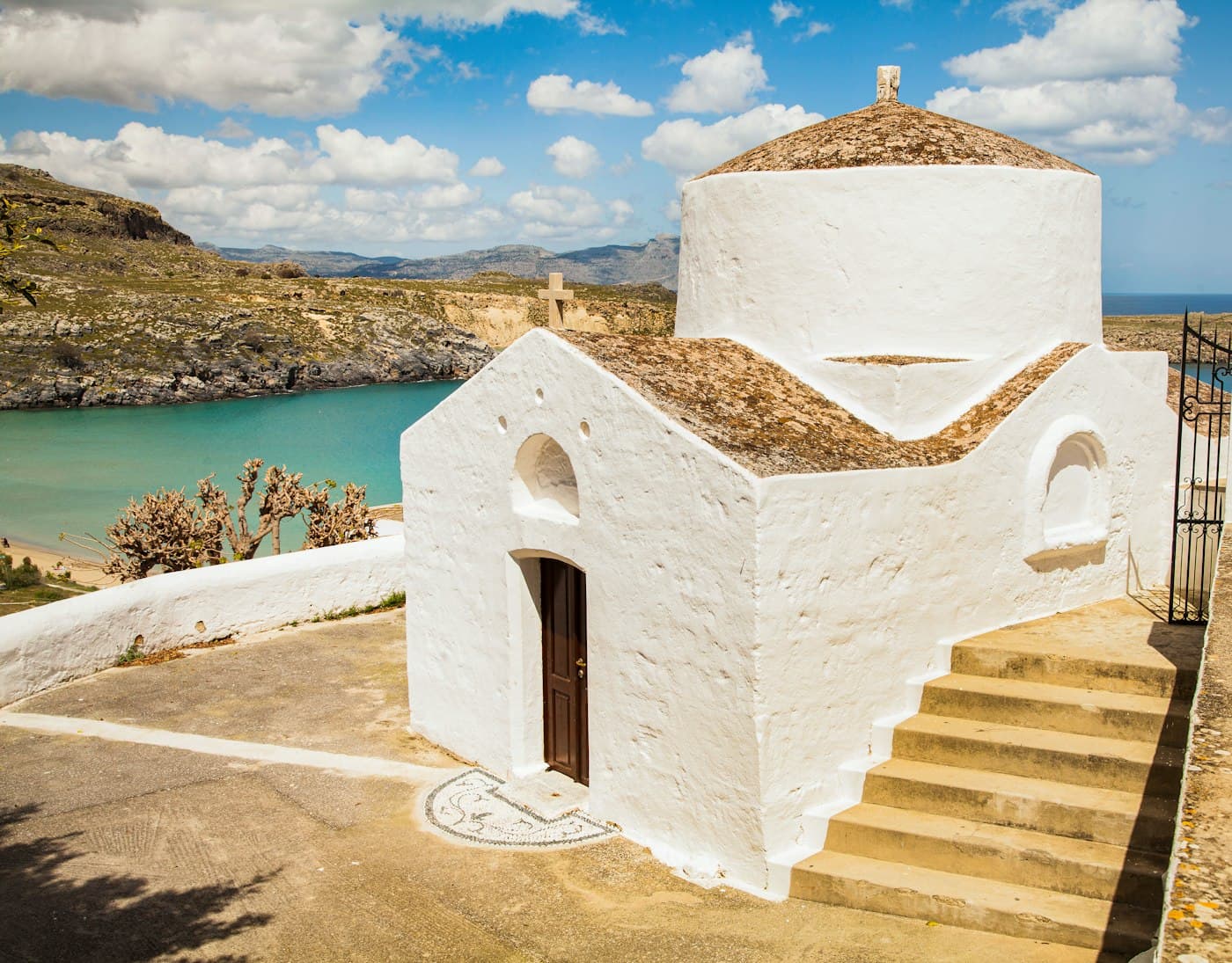 The whitewashed chapel of Agios Georgios Pachymachiotis above Lindos, steps up to its door, the turquoise bay and the hills of Rhodes behind