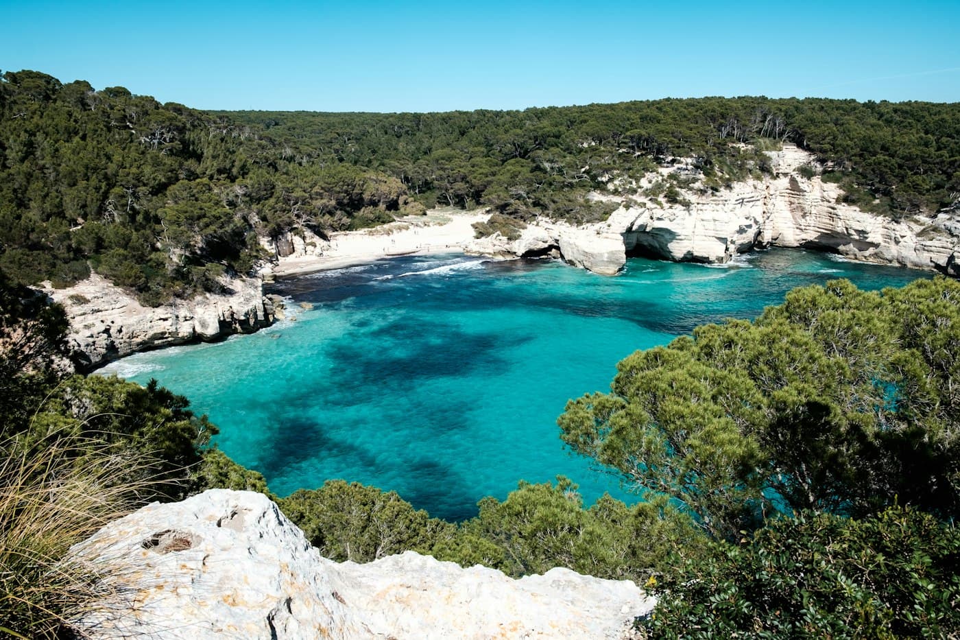 Cala Mitjana desde el acantilado: agua turquesa, roca caliza blanca y pinos