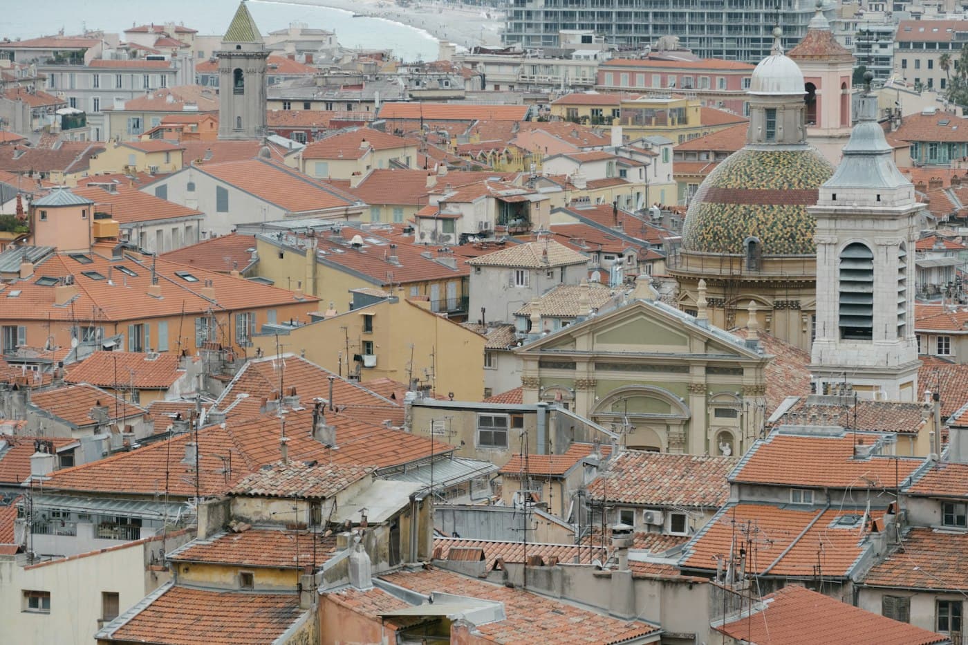 The roofs of Old Nice with the glazed-tile dome and the bell tower of Sainte-Réparate cathedral, the beach and the sea beyond