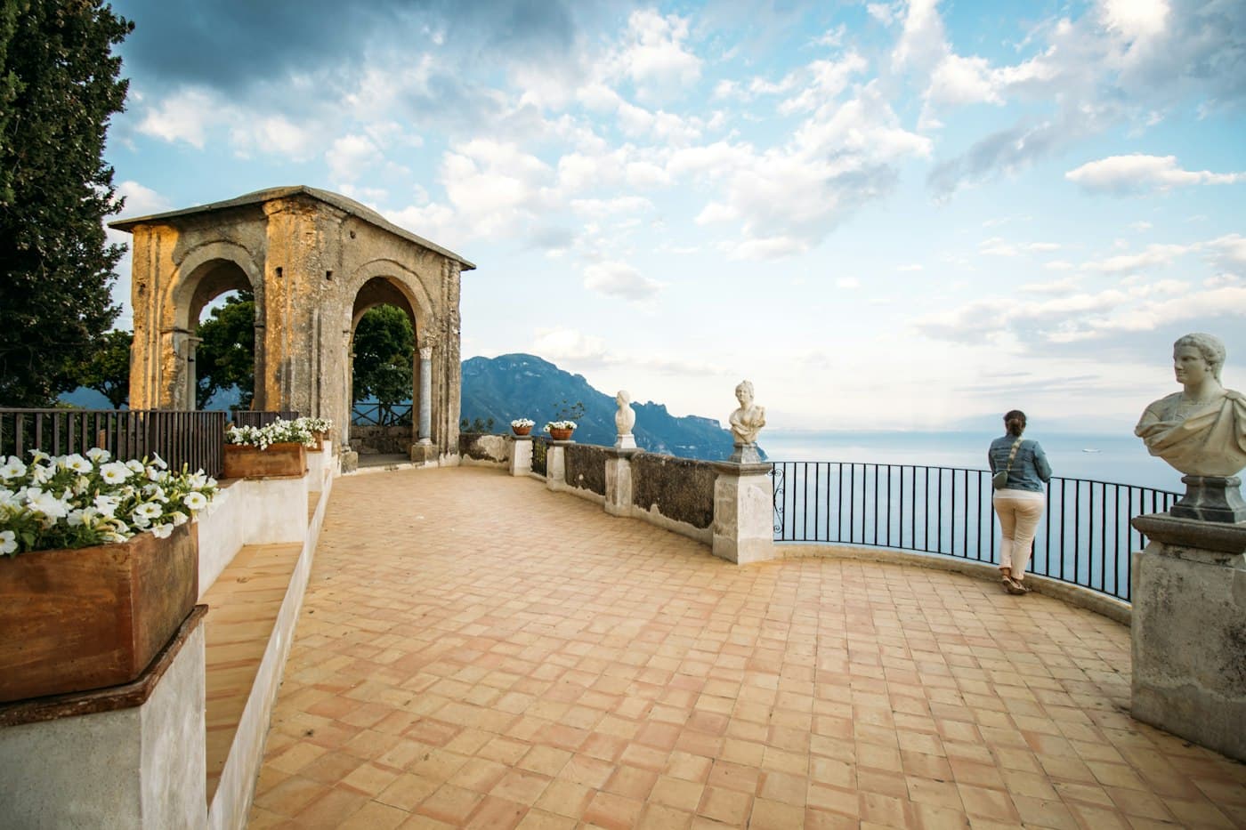 Una terrazza con busti di marmo e un padiglione in pietra a picco sul mare a Ravello, una visitatrice alla ringhiera