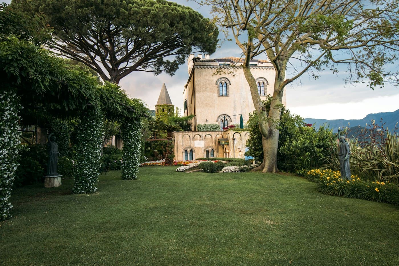 Un prato con statue e un pergolato coperto di fiori bianchi davanti a un’antica villa a Ravello