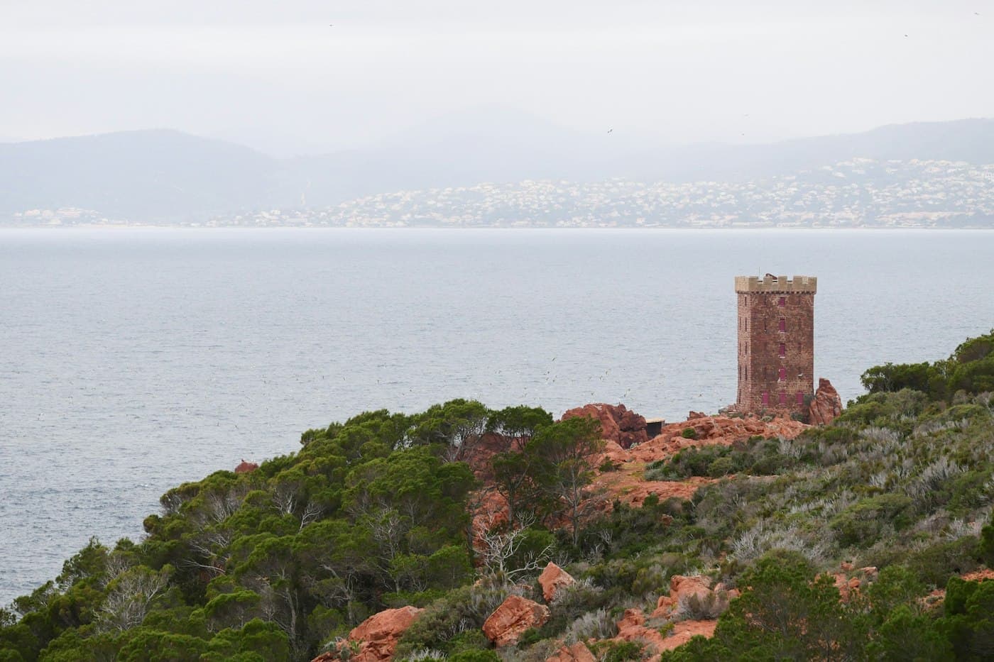 The crenellated tower of the Île d’Or off Cap Dramont, above pines and red rocks, with the gulf and a far shore in soft grey light
