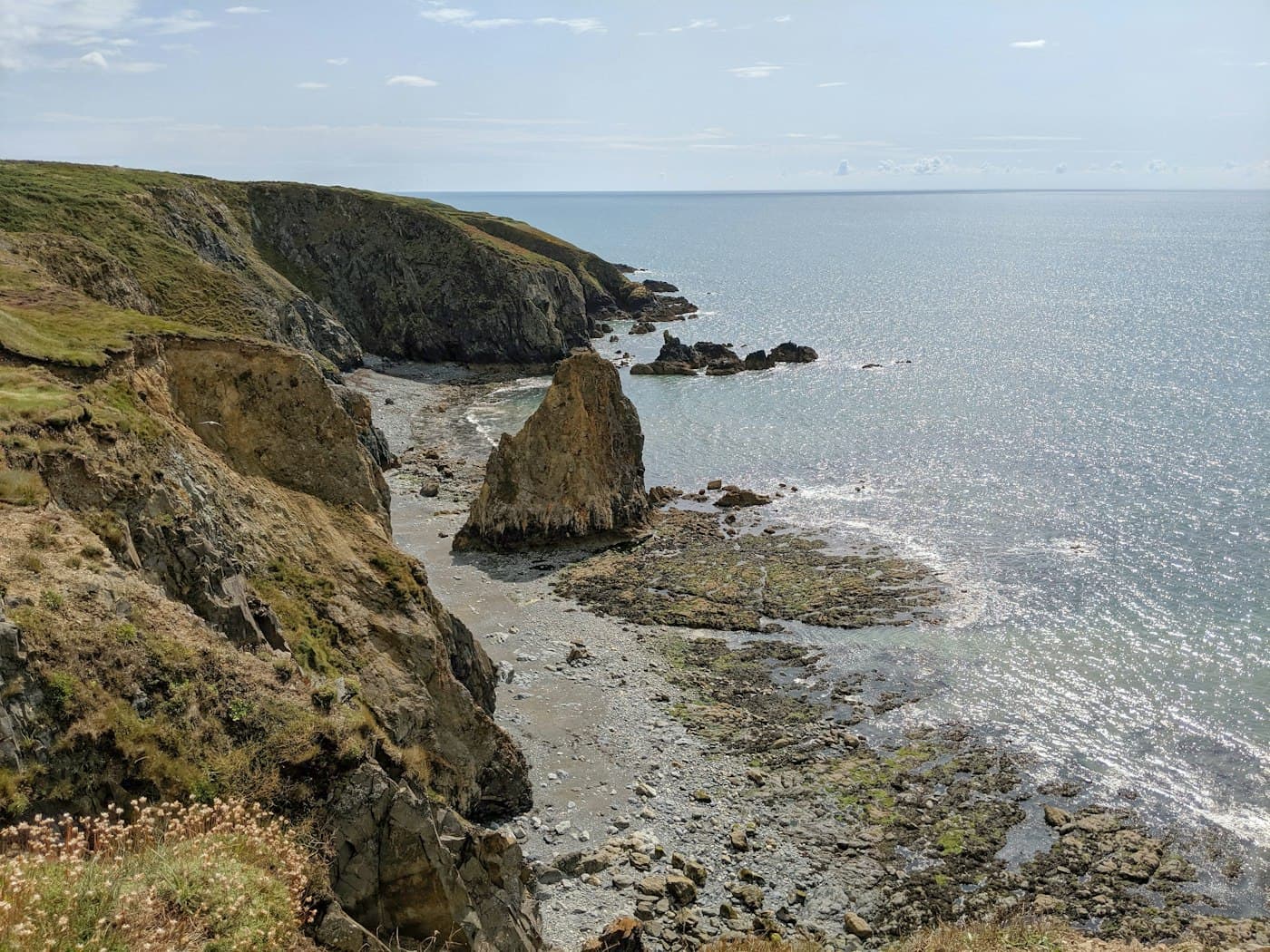 Un faraglione su una riva rocciosa ai piedi delle scogliere della Copper Coast, nella contea di Waterford, con il mare che scintilla al sole
