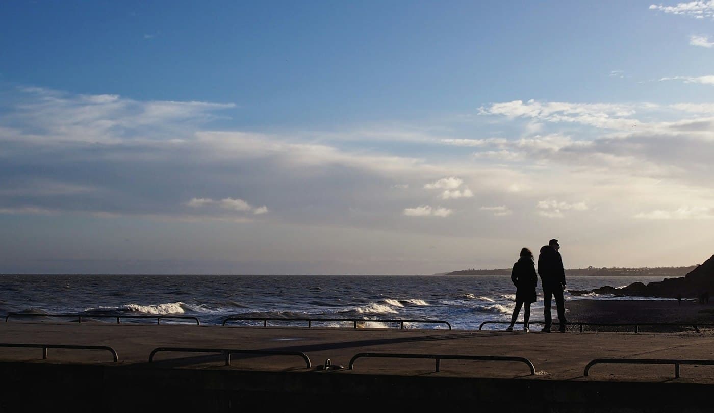 Una coppia in controluce sul lungomare di Courtown, nella contea di Wexford, a guardare le onde che si infrangono nella luce bassa d’inverno