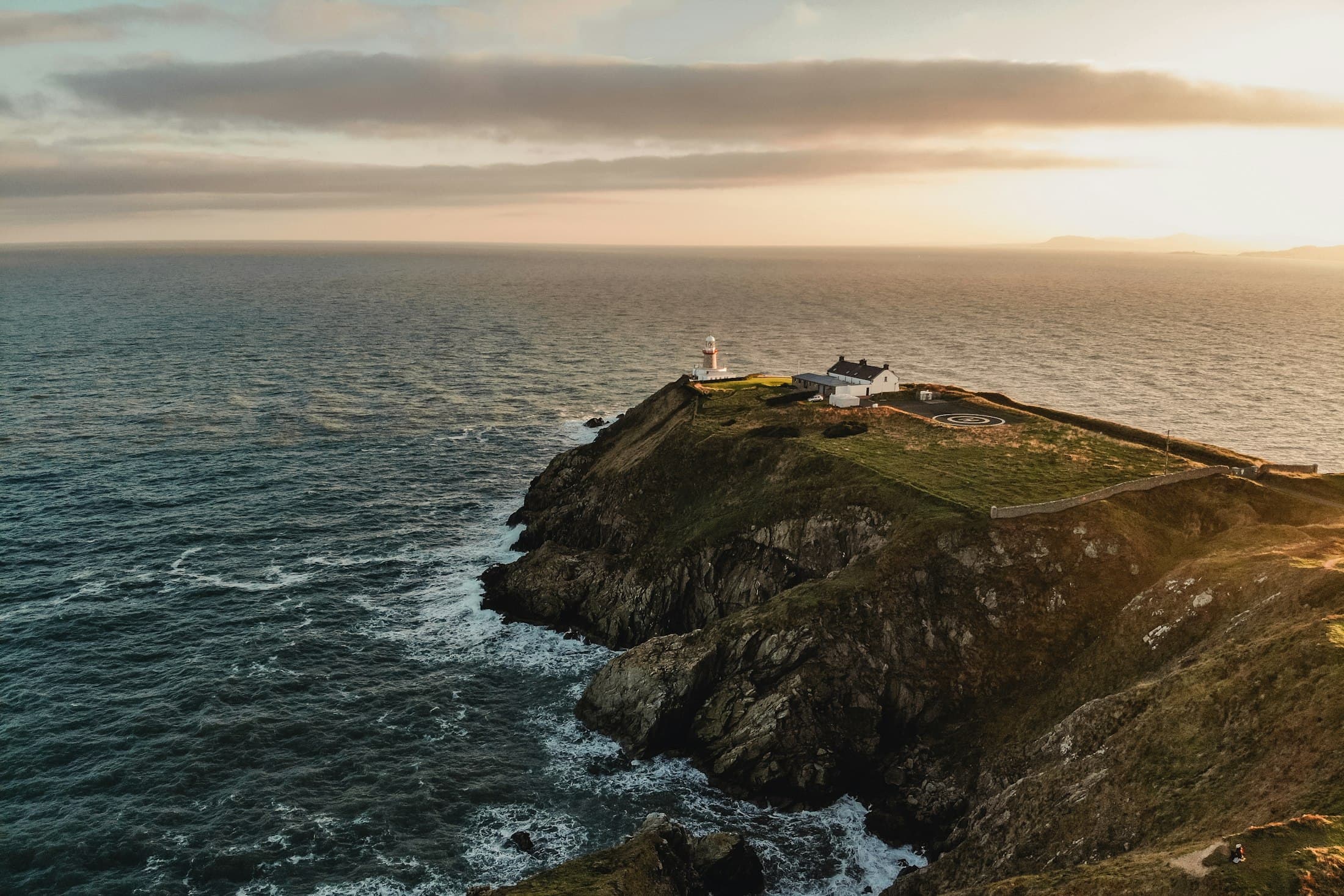 The Baily lighthouse at the tip of Howth Head seen from above at sunset, with cliffs and the open sea around it