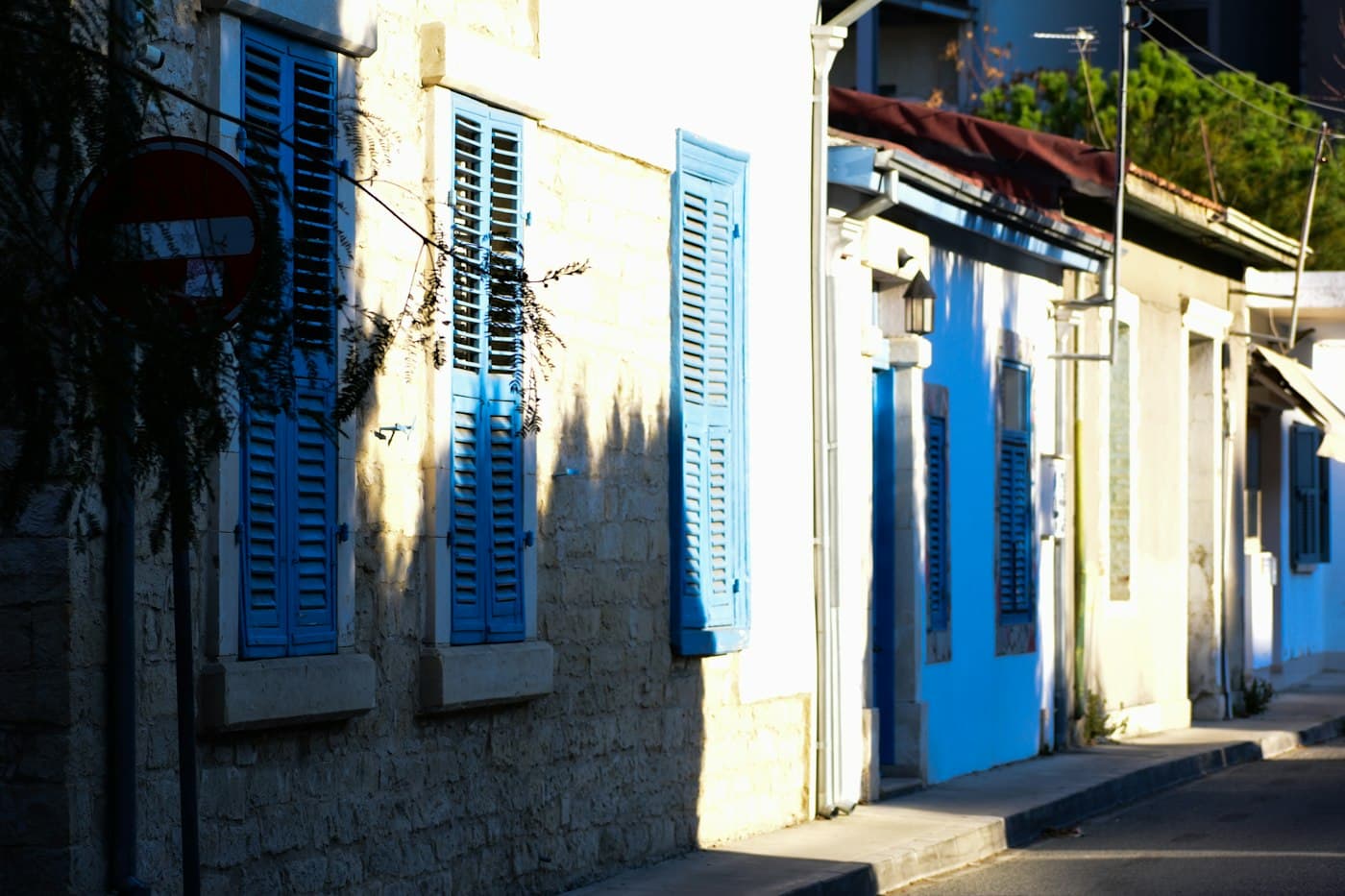 Steinhäuser mit blauen Holzläden in einer ruhigen Straße der Altstadt von Limassol, in tiefer Nachmittagssonne