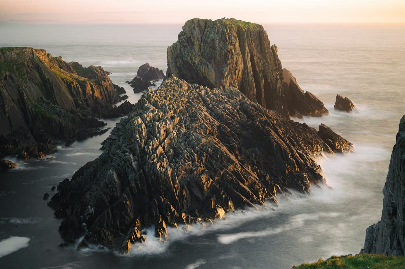 Jagged rocks and sea stacks at Malin Head in the low evening sun, with the sea blurred white around them