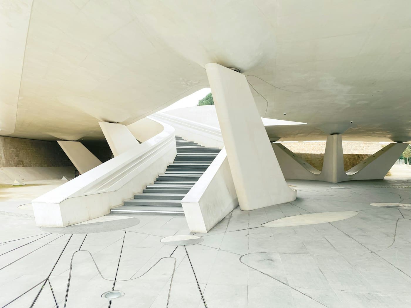 Weiße Betontreppen und schräge Stützen unter dem Eleftheria-Platz in Nikosia, dahinter die alte Steinmauer des Grabens