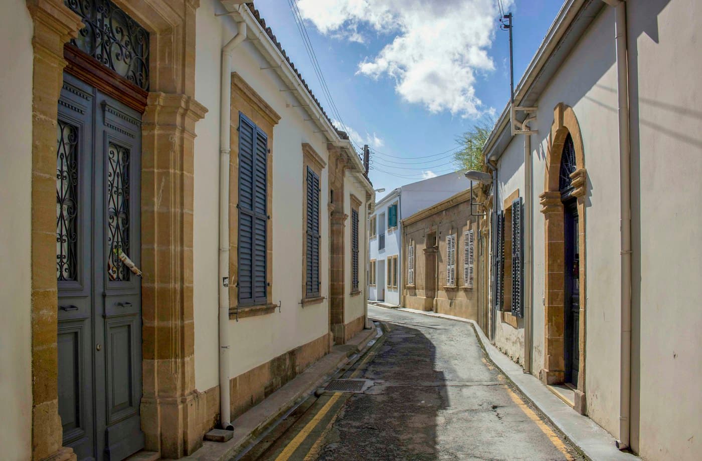 Eine schmale Straße mit alten Häusern in Nikosia, hohen Fenstern mit Fensterläden und Türen in honigfarbenen Steinrahmen