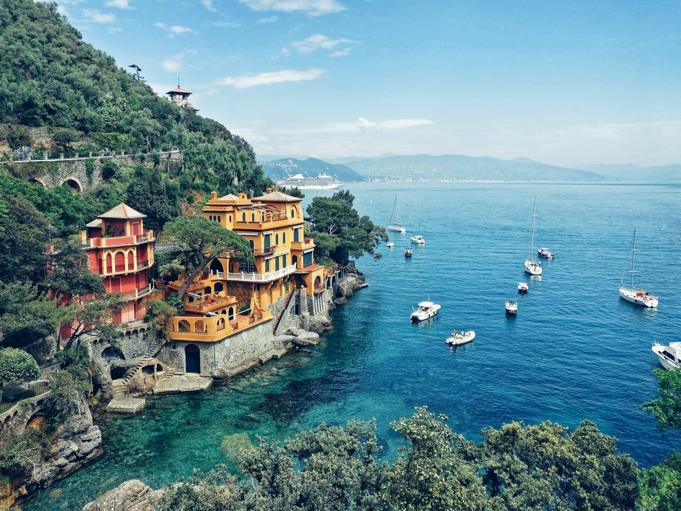 Rote und ockerfarbene Villen auf den Felsen über einer Bucht mit klarem Wasser bei Portofino, in der Boote vor Anker liegen