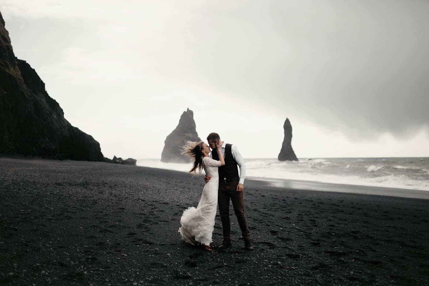 Due sposi che si baciano sulla sabbia nera di Reynisfjara, con i faraglioni di Reynisdrangar alle spalle