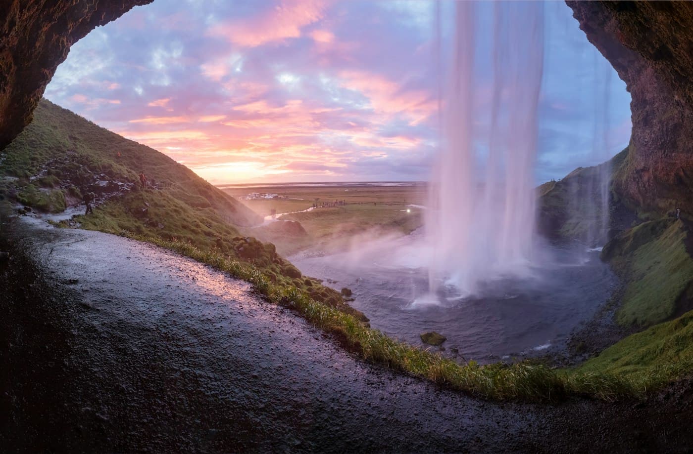 La vista da dietro Seljalandsfoss al tramonto, con l’acqua che cade davanti a un cielo rosa