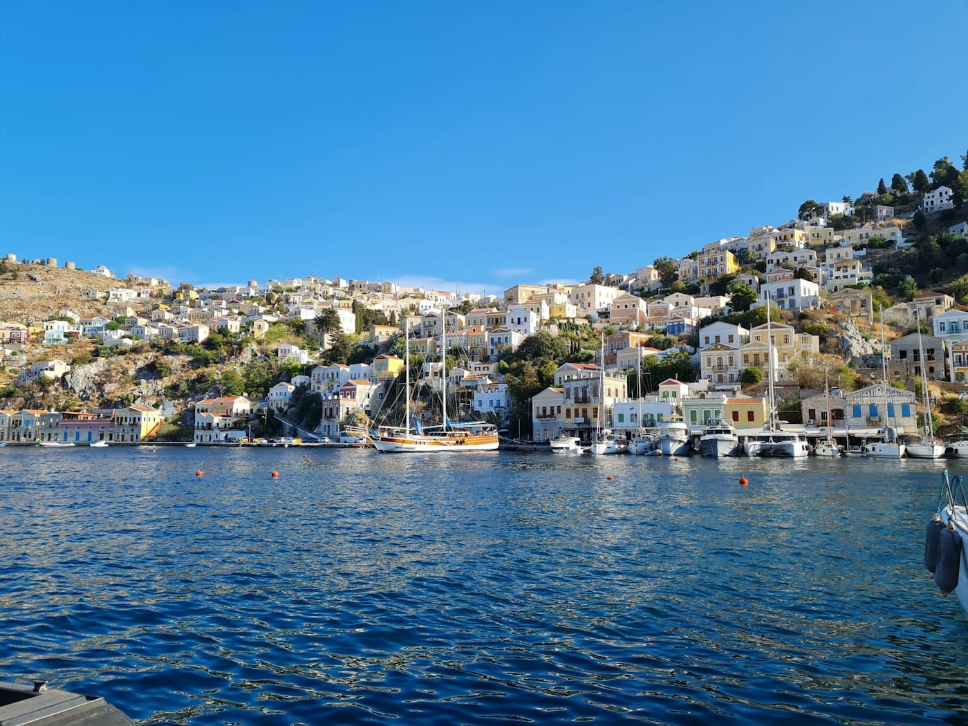 Des maisons pastel étagées sur les collines autour du port de Symi, des voiliers à quai